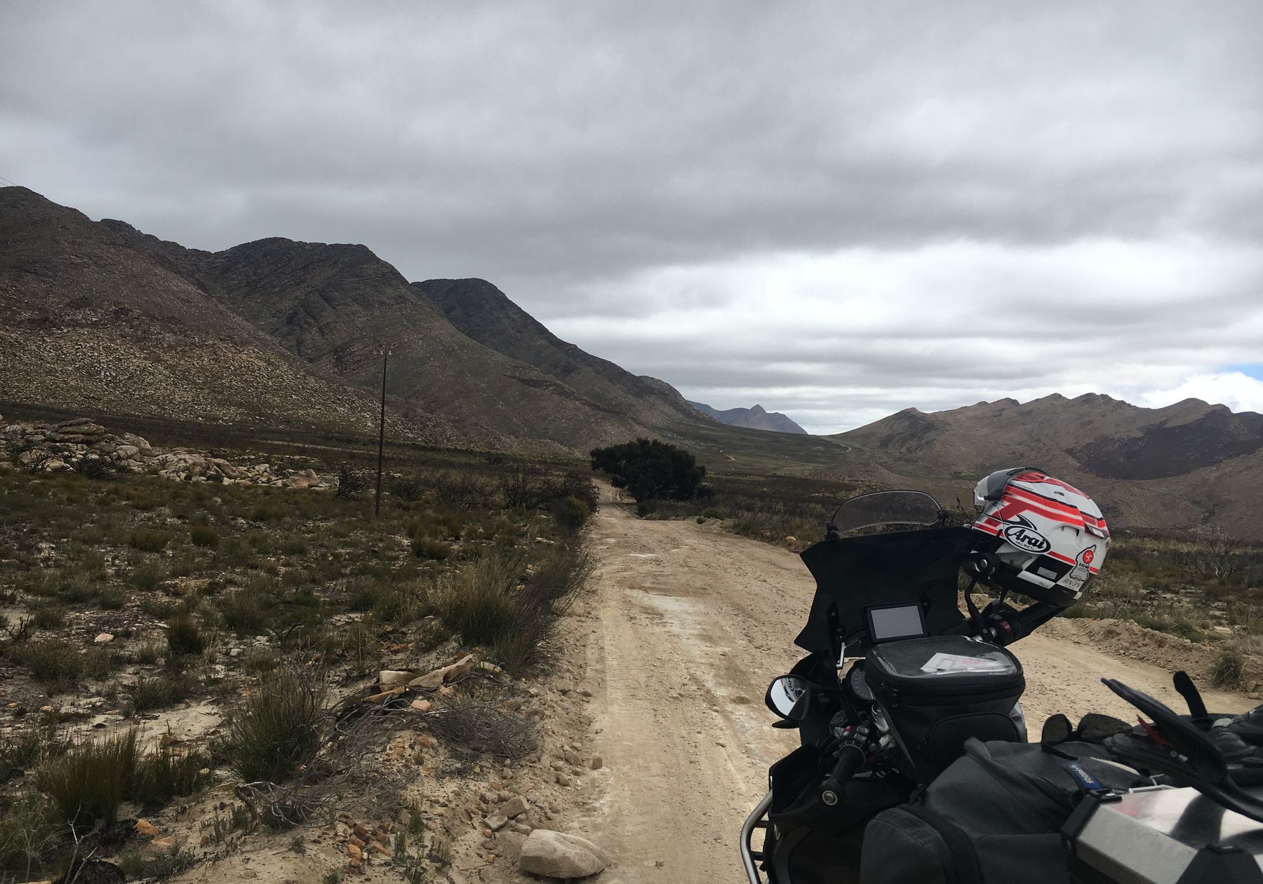 A gravel road winding through the Swartberg mountains, motorcycle in the foreground